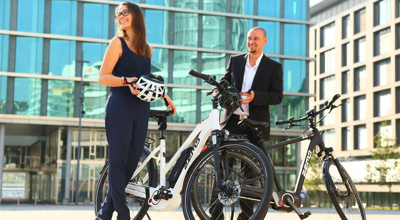 Ein und eine Frau mit jeweils einem E-Bike vor einem Geschäftsgebäude