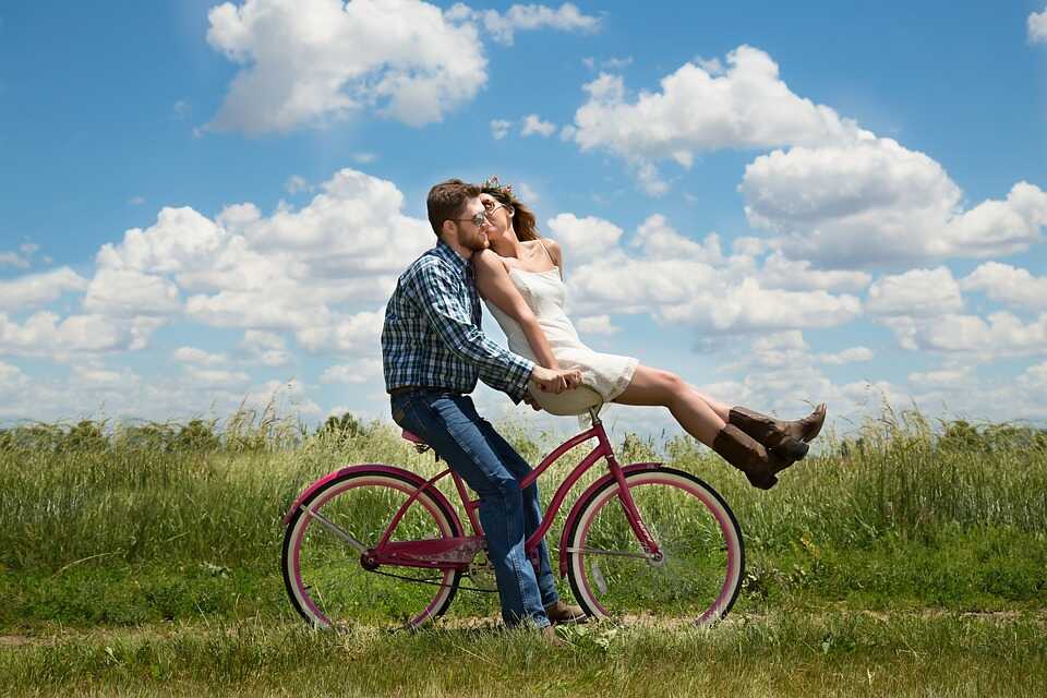 Tipps zum Fahrradfahren Ein Mann sitzt auf einem pinken Cityrad. Auf dessen Fahrrad Lenker sitzt eine Frau